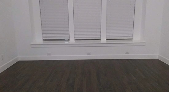 Empty room with dark wood floors, white walls, and three windows with blinds.