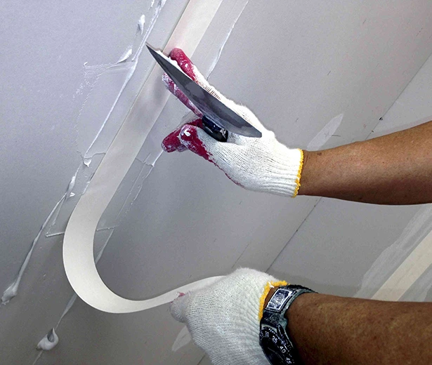 Applying drywall tape during an emergency drywall repair job. Close-up of hands with a taping knife.