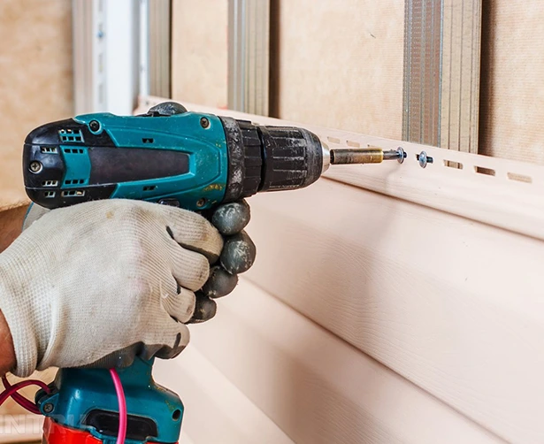 Installing custom home siding with a power drill. Close-up of siding installation.