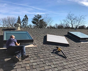 Man replacing a skylight on a shingled roof.