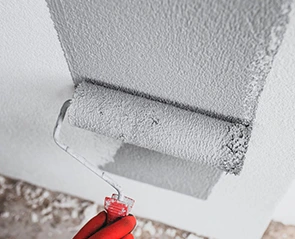 Paint roller applying gray paint to a wall, relevant to water damage repair projects.